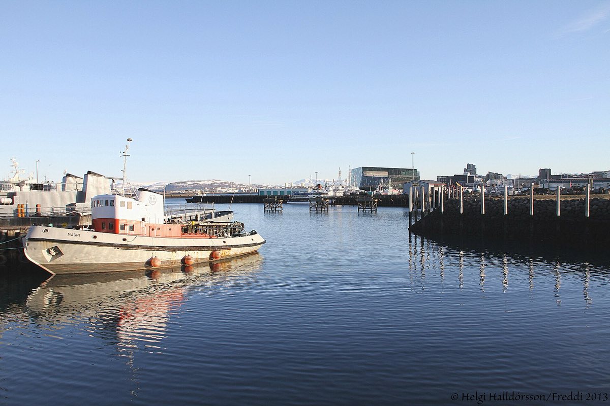 Gamla höfnin í Reykjavík: bátur við bryggju, borgin og fjöllin í baksýn.
